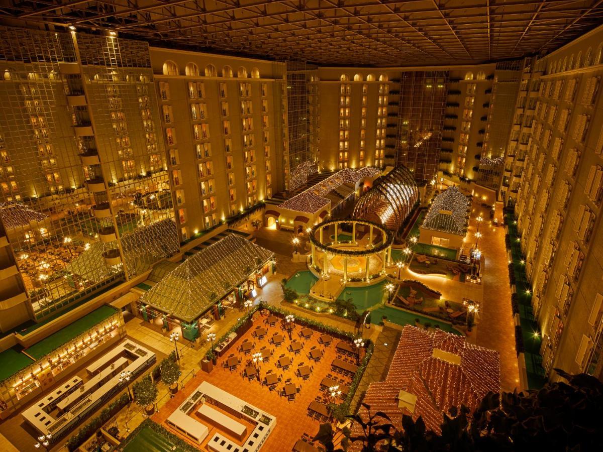 Grand Nikko Tokyo Bay Maihama Urayasu Exterior foto The photo shows a large, illuminated atrium of a hotel or resort complex. Several floors of what appear to be guest rooms or apartments surround the central area. The atrium contains a variety of amenities, including a pool or water feature, landscap