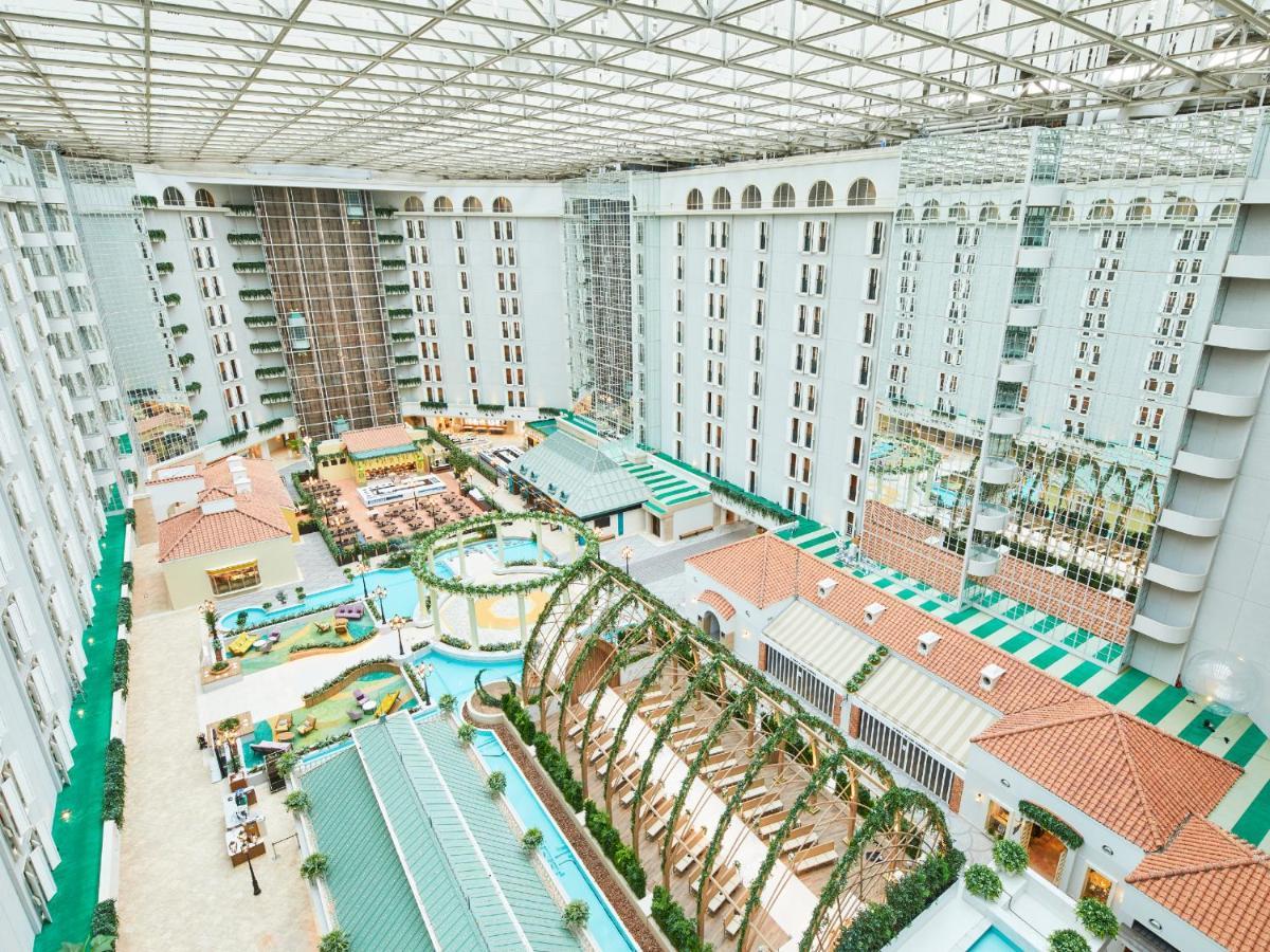 Grand Nikko Tokyo Bay Maihama Urayasu Exterior foto The photo shows a large indoor space, likely a hotel or resort atrium. The area features multiple levels of buildings surrounding a central courtyard. This courtyard includes various amenities such as pools, landscaped gardens, and recreational areas