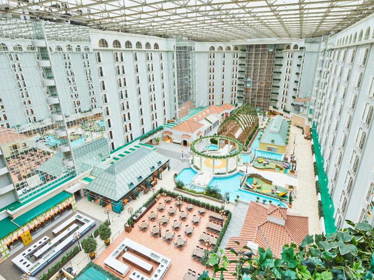 Grand Nikko Tokyo Bay Maihama Urayasu Exterior foto The photo depicts a large indoor area, likely within a resort or hotel, featuring a spacious atrium. The atrium has a glass roof, allowing natural light to flood the space. In the center, there are various swimming pools and a lush, green landscape w