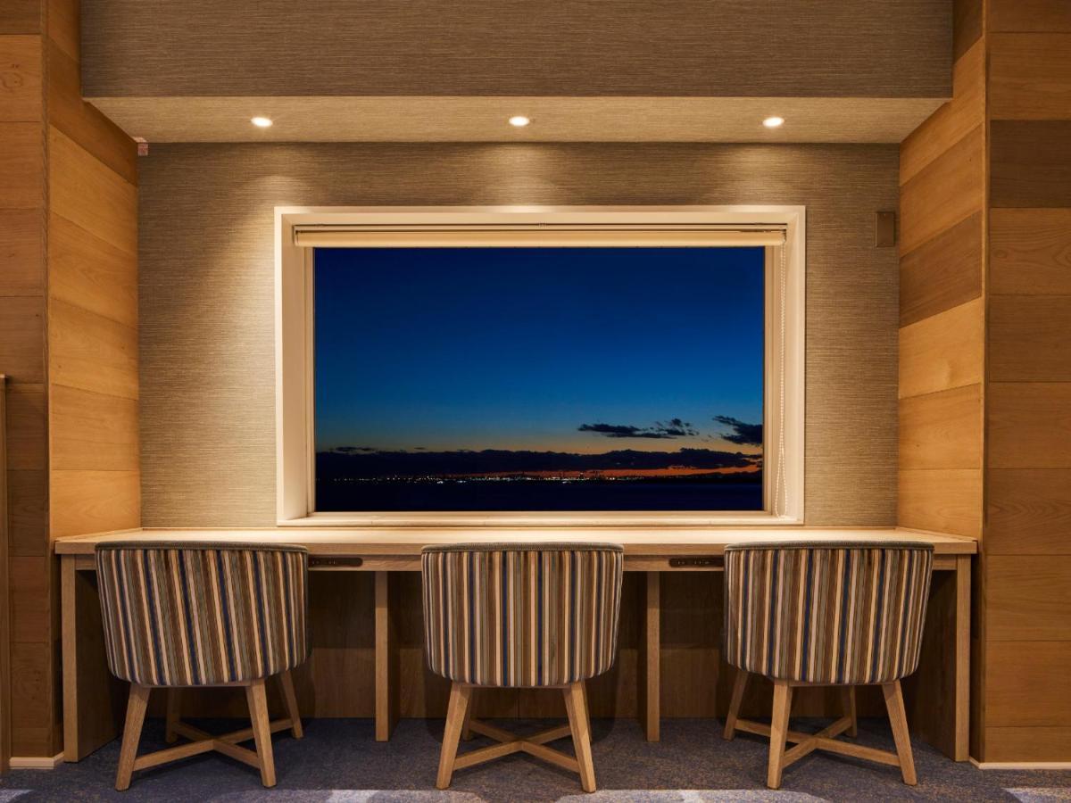 Grand Nikko Tokyo Bay Maihama Urayasu Exterior foto The photo depicts a cozy workspace or study area featuring a long, minimalist desk with three chairs. The wall behind the desk is made of wood, creating a warm atmosphere. At the center, there is a large window that showcases a beautiful evening view