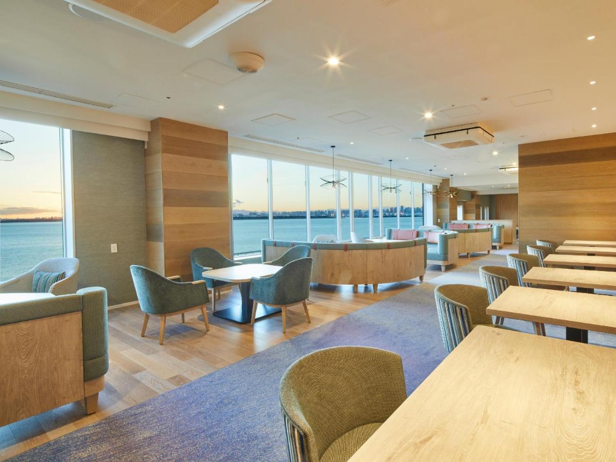 Grand Nikko Tokyo Bay Maihama Urayasu Exterior foto The photo shows a modern interior space, likely a dining or lounge area. It features large windows that offer a view of the water, allowing natural light to fill the room. The decor includes wooden walls and stylish, comfortable furniture, with sever