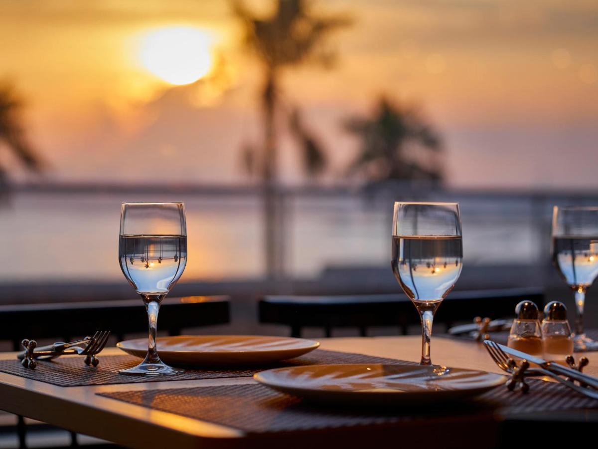 Grand Nikko Tokyo Bay Maihama Urayasu Exterior foto The photo depicts a picturesque dining setting at sunset. In the foreground, there are two elegantly arranged tables, each set with plates and glasses filled with water. The glasses are crystal clear, reflecting the warm colors of the sunset. Behind 