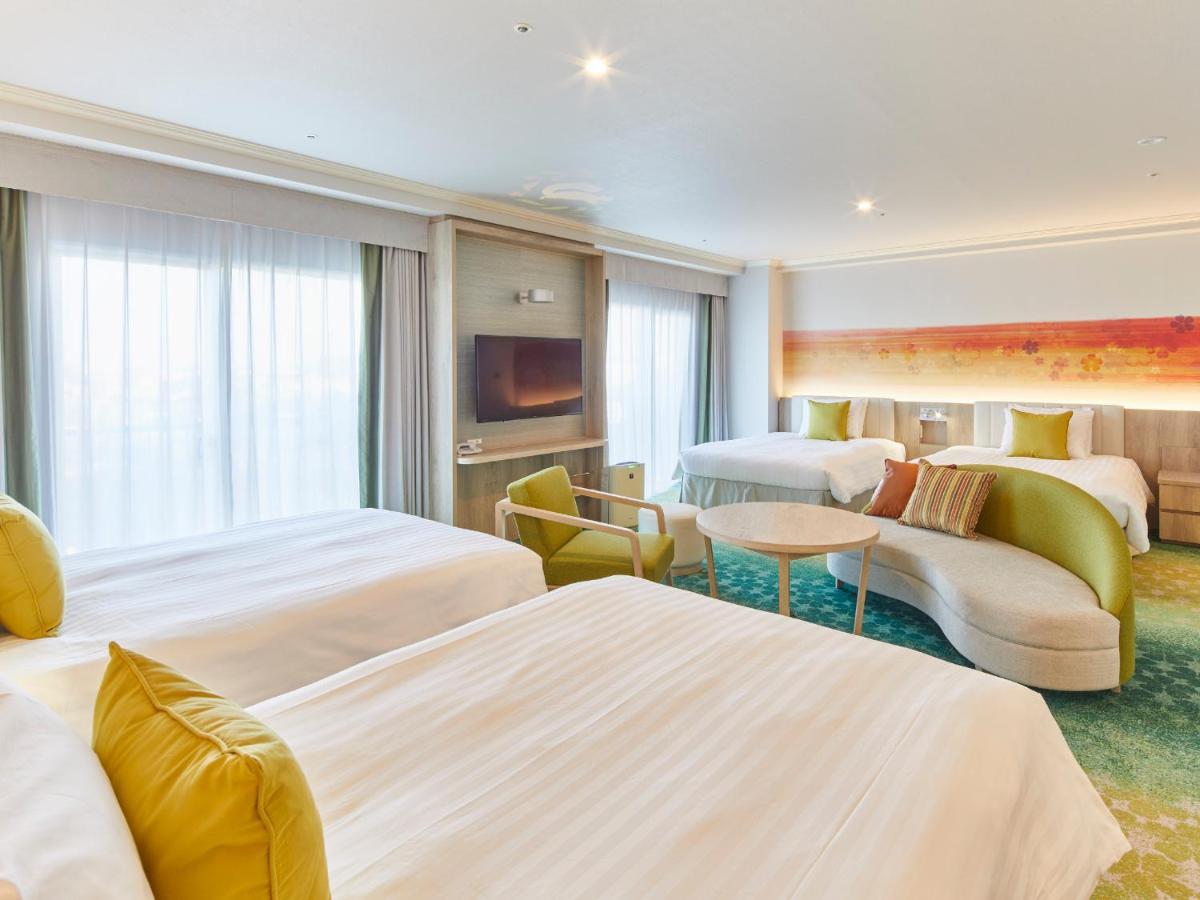 Grand Nikko Tokyo Bay Maihama Urayasu Exterior foto The photo shows a modern hotel room that features two large beds covered with white bedding and decorative pillows. There is a contemporary, curved sofa in a light color, along with a round table in the middle. The room has large windows that allow n