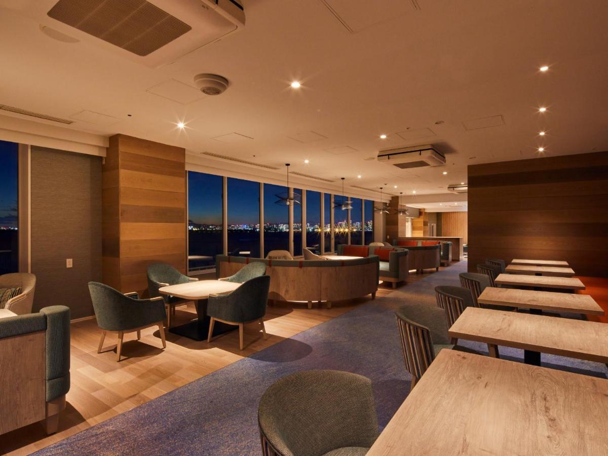 Grand Nikko Tokyo Bay Maihama Urayasu Exterior foto The photo shows a modern, well-lit lounge or café area. It features a mix of seating options, including cozy armchairs and tables with chairs. The space has large windows displaying a view, likely of a city or landscape at dusk, given the nighttime a