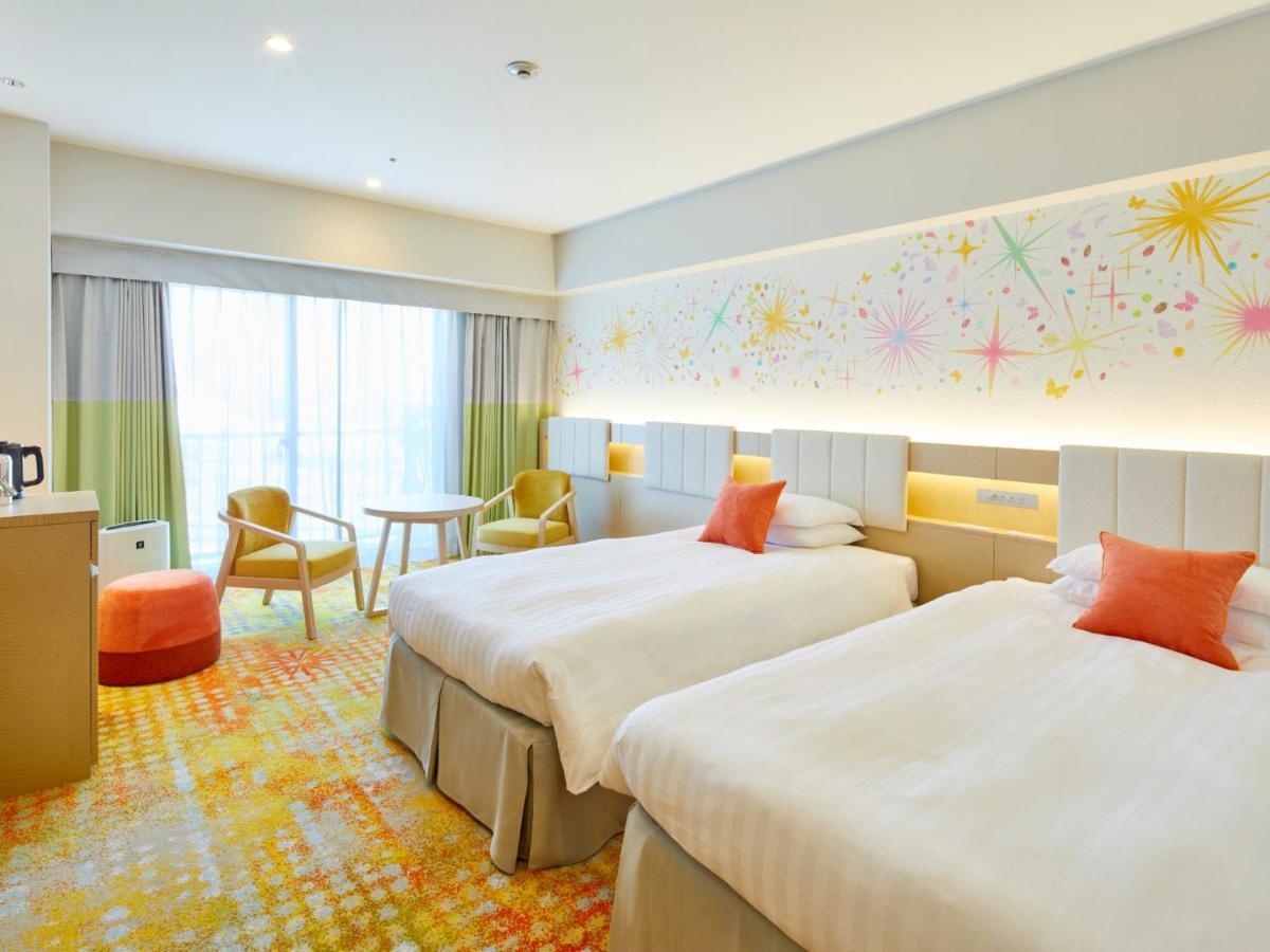 Grand Nikko Tokyo Bay Maihama Urayasu Exterior foto The photo shows a modern hotel room featuring two twin beds with light-colored bedding and decorative orange cushions. There is a vibrant, colorful carpet on the floor, and the walls are adorned with playful designs, including bursts of color. A larg