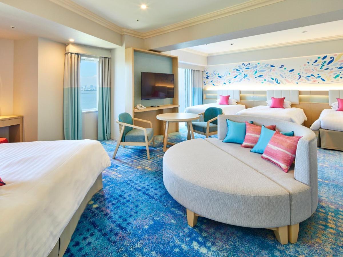 Grand Nikko Tokyo Bay Maihama Urayasu Exterior foto The photo shows a modern hotel room featuring a spacious layout with multiple beds. There is a large, curved sofa with colorful cushions in the center, adding a contemporary touch to the design. The room has large windows allowing natural light to fi