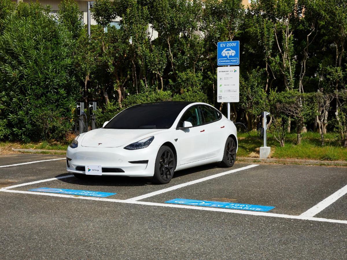 Grand Nikko Tokyo Bay Maihama Urayasu Exterior foto The photo shows a white electric car parked in an EV (electric vehicle) charging spot. The car has a sleek design with black wheels and tinted windows. In the background, there are green shrubs and trees, indicating a natural or landscaped environmen
