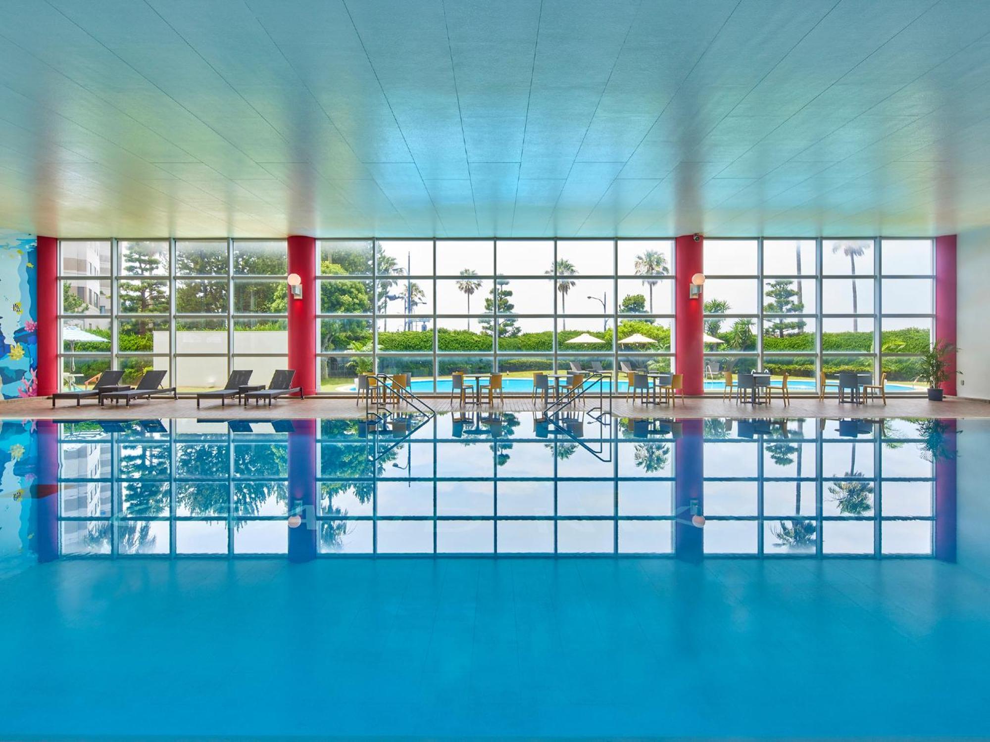 Grand Nikko Tokyo Bay Maihama Urayasu Exterior foto The photo shows an indoor swimming pool with bright blue water. The pool area is spacious, characterized by large windows that allow natural light to flood in, creating a vibrant atmosphere. The walls are painted in a soft color, with accents of red.