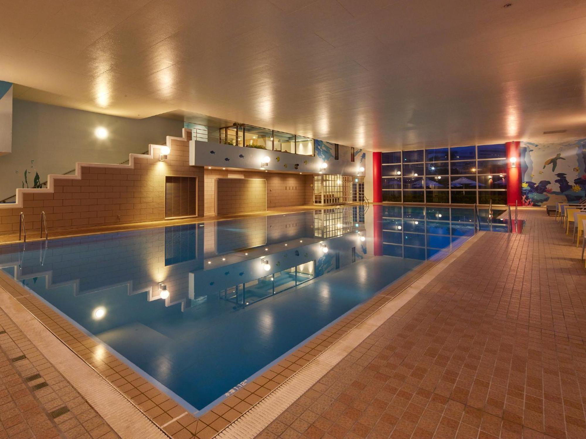 Grand Nikko Tokyo Bay Maihama Urayasu Exterior foto The photo shows an indoor swimming pool area. The pool features a calm blue water surface and is surrounded by tiled flooring. There is a staircase leading to a higher level, likely providing access to a lounge or seating area. Large windows allow na