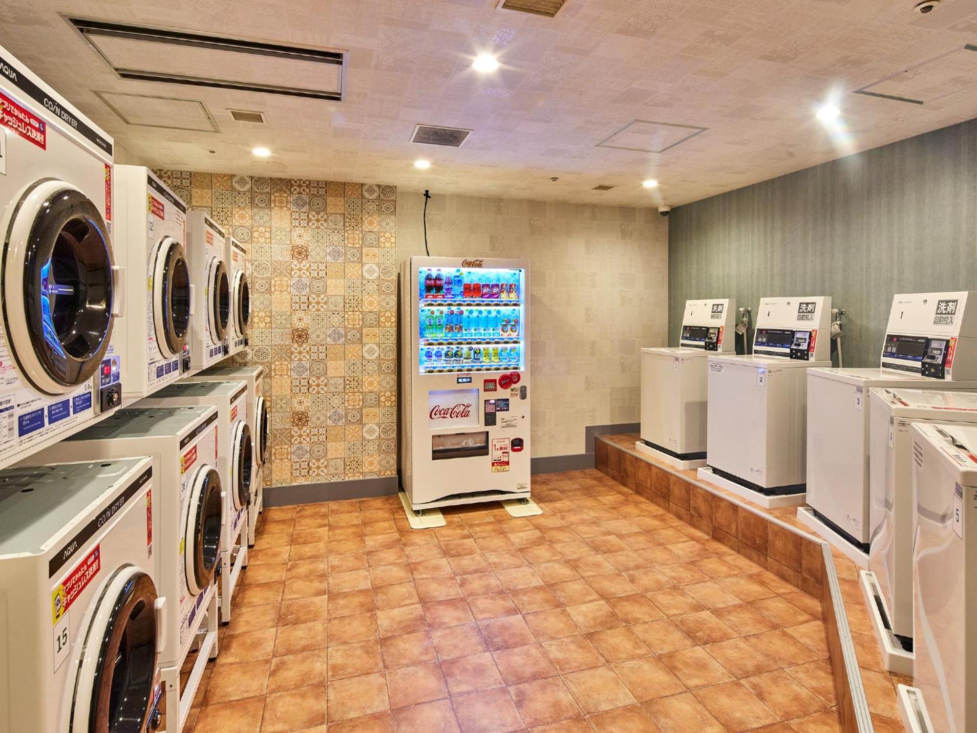 Grand Nikko Tokyo Bay Maihama Urayasu Exterior foto The photo shows a laundry room equipped with several washing machines and dryers. On the left side, there are multiple front-loading washing machines arranged in a row, and on the right side, there are dryers. In the center, there is a vending machin